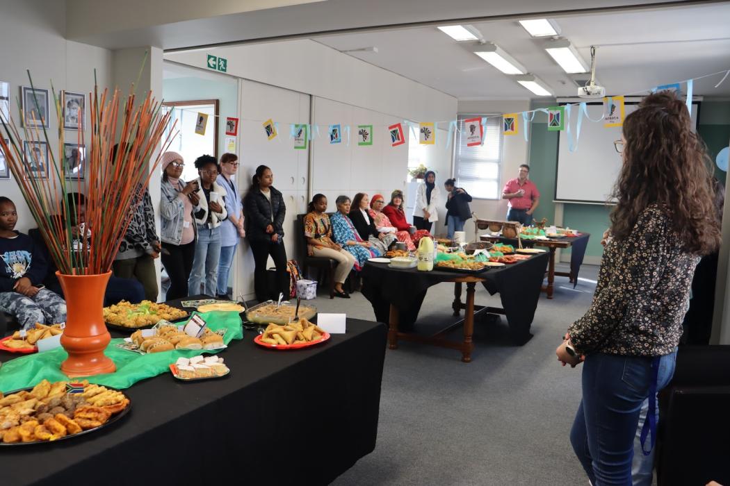 A room filled with people on the sides and tables filled with treats from different African countries.
