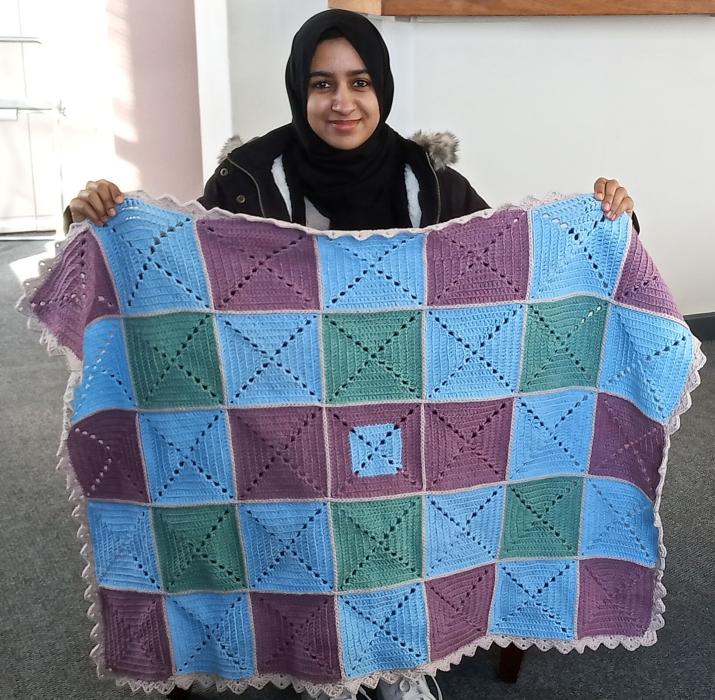 A student holding up her knitted blanket