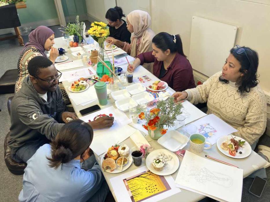 A group of people seated around a table with various dishes, beverages, and colorful flowers, in a casual dining setting.