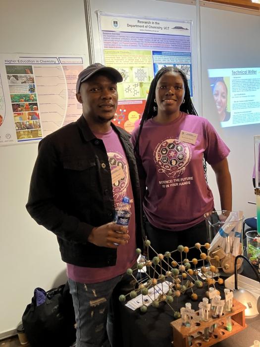 Two postgraduate students pose in front of the chemistry exhibition