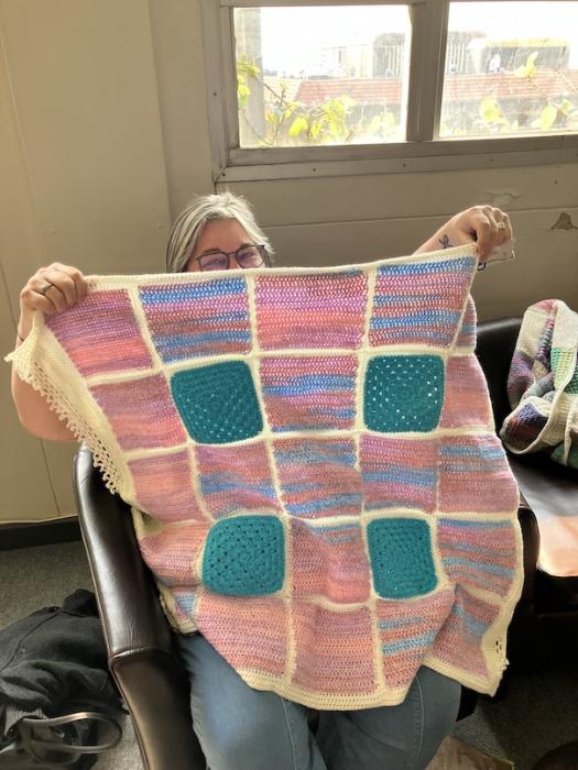 woman with glasses holding up a pink and blue knitted blanket