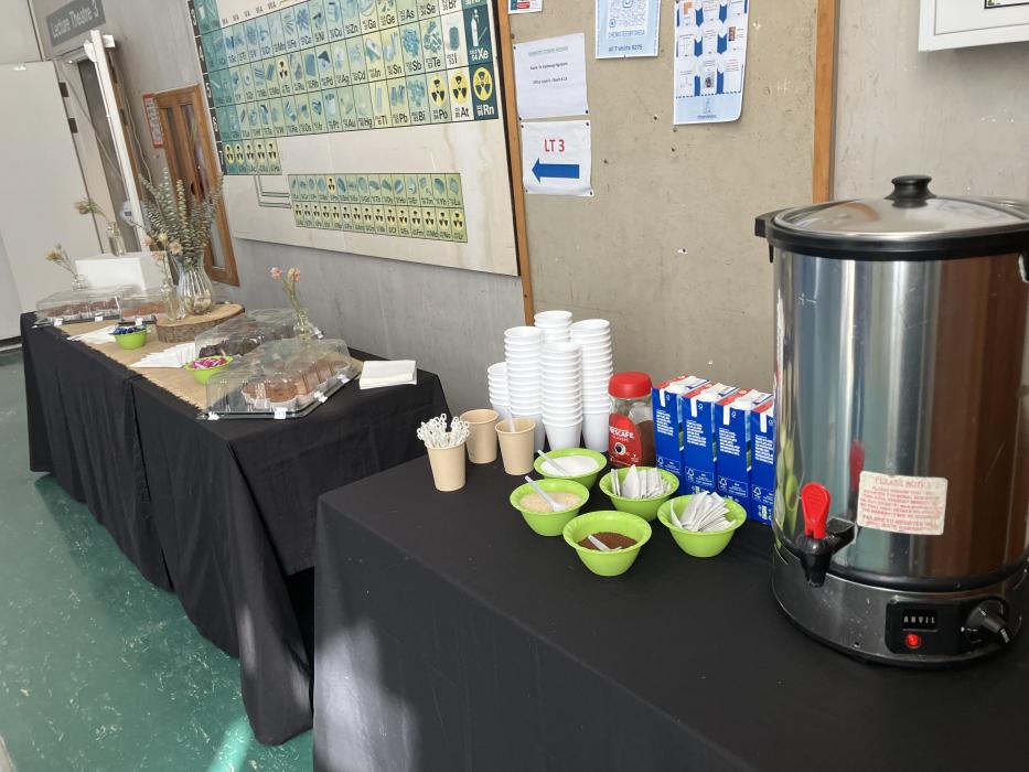 “Refreshment table with snacks and beverages in a hallway with informational posters.”