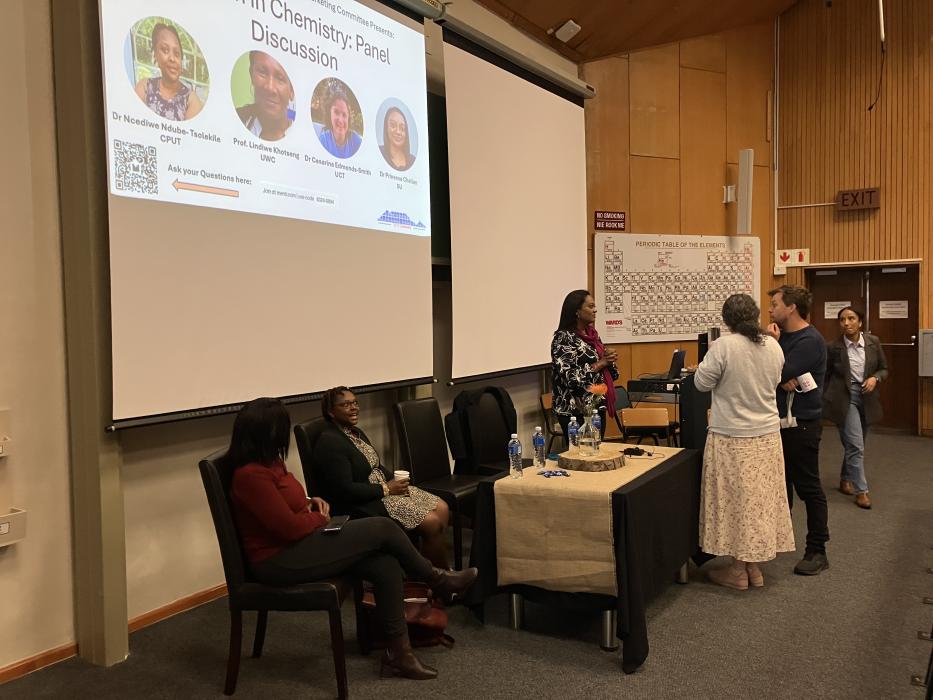 Panel discussion at a chemistry event with audience members and a whiteboard with notes.
