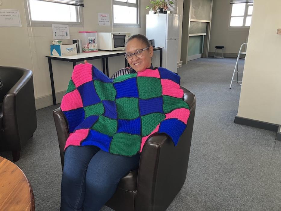 Woman holding a blue, green and pink knitted blanket