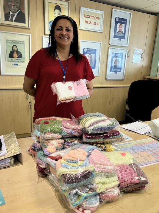Woman standing in front of donated tiny knitted beanies and vests