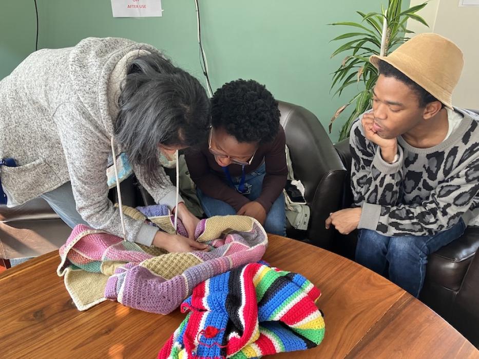 A woman shows another woman her knitting while a man looks on