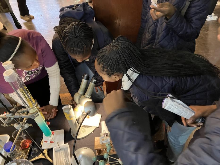 A postgraduate student shows interested learners a crystal using a microscope