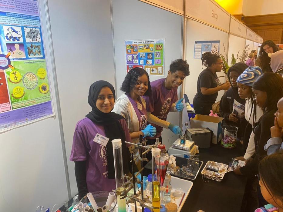 Three chemistry department postgraduate students pose in front of the chemistry exhibition