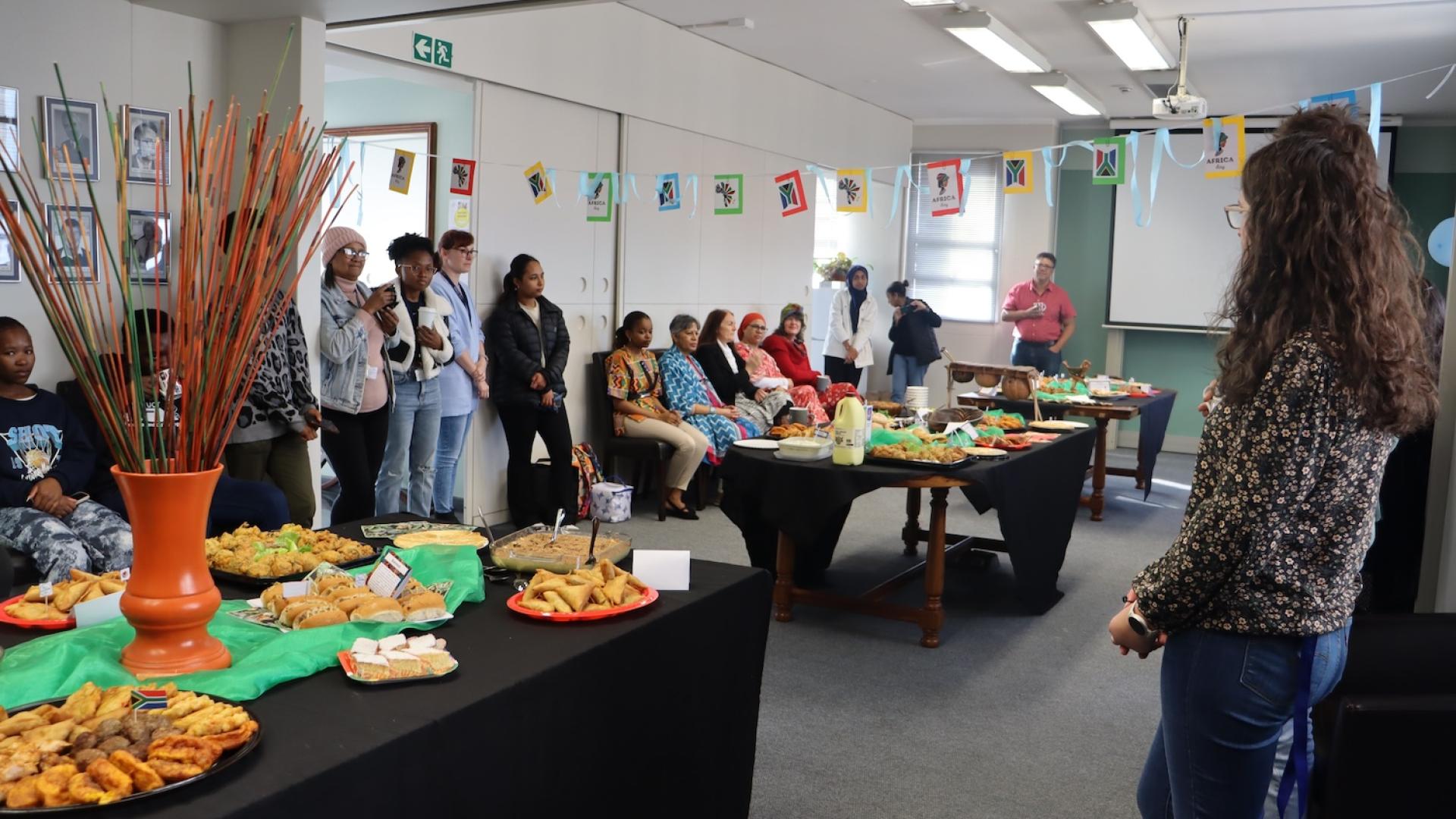 A room filled with people on the sides and tables filled with treats from different African countries.