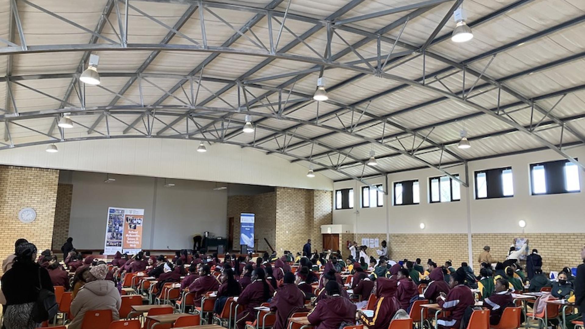Large hall filled with female learners, teachers and exhibitors