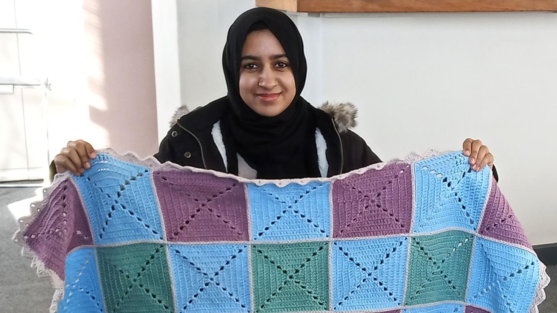 A student holding up her knitted blanket
