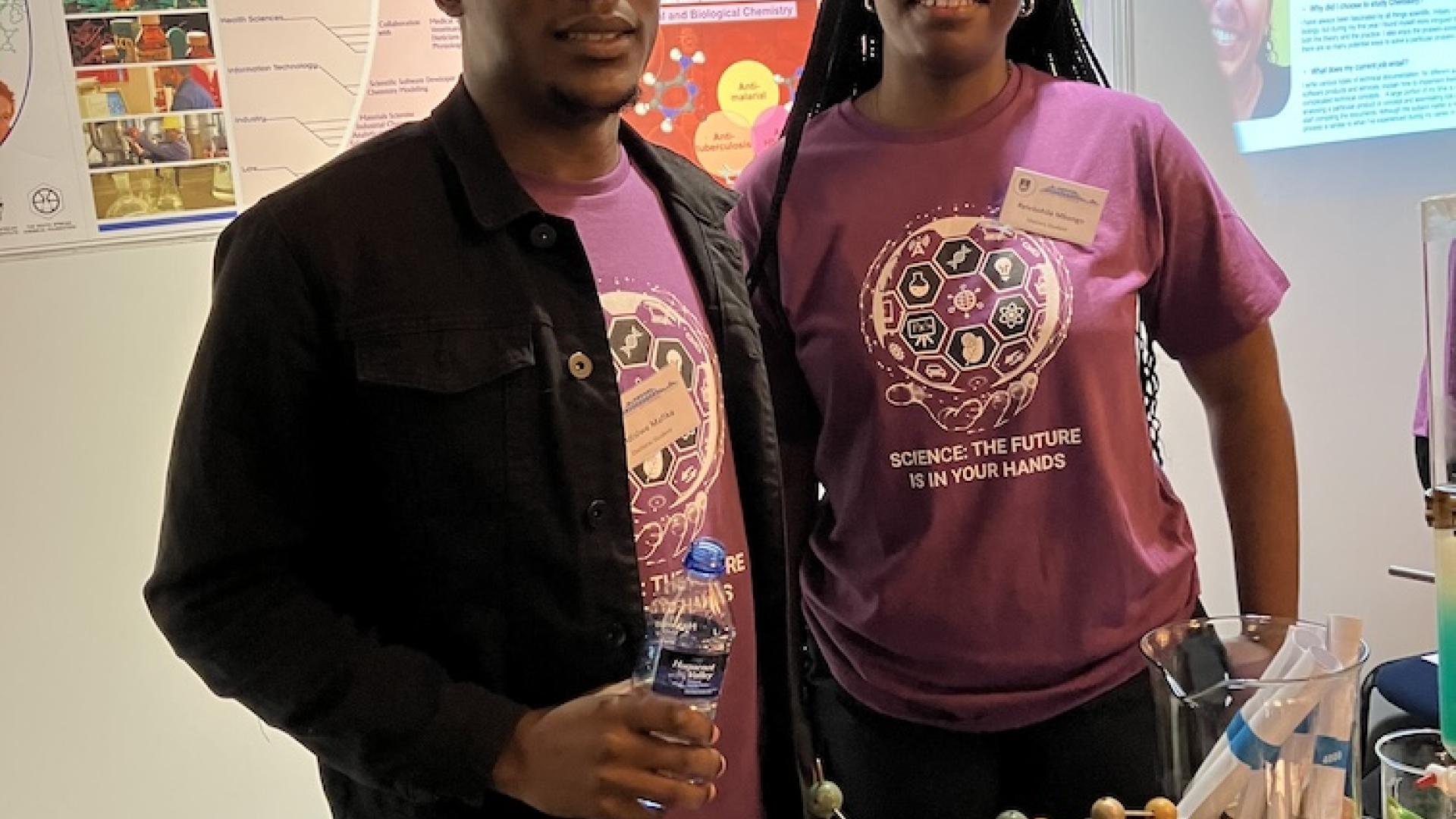 Two postgraduate students pose in front of the chemistry exhibition