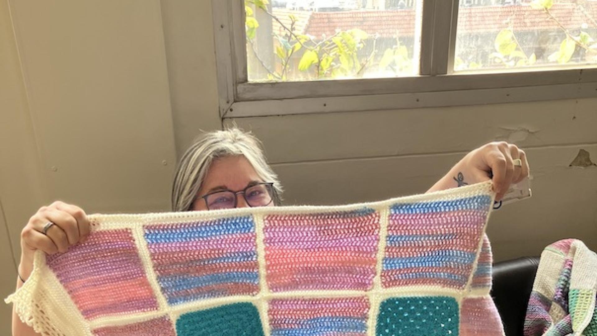 woman with glasses holding up a pink and blue knitted blanket