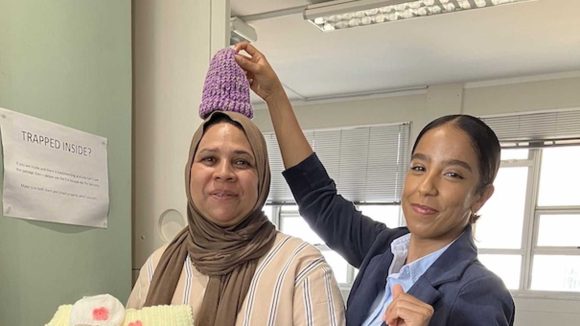 Woman playfully holds a knitted beanie over her colleague's head