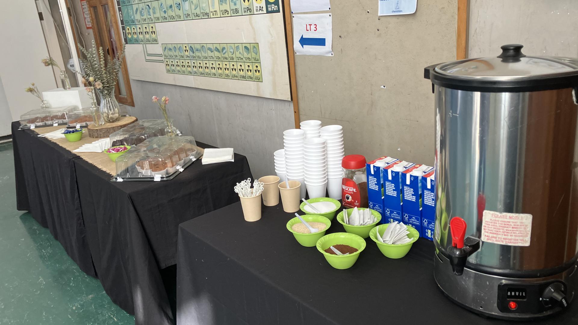 “Refreshment table with snacks and beverages in a hallway with informational posters.”
