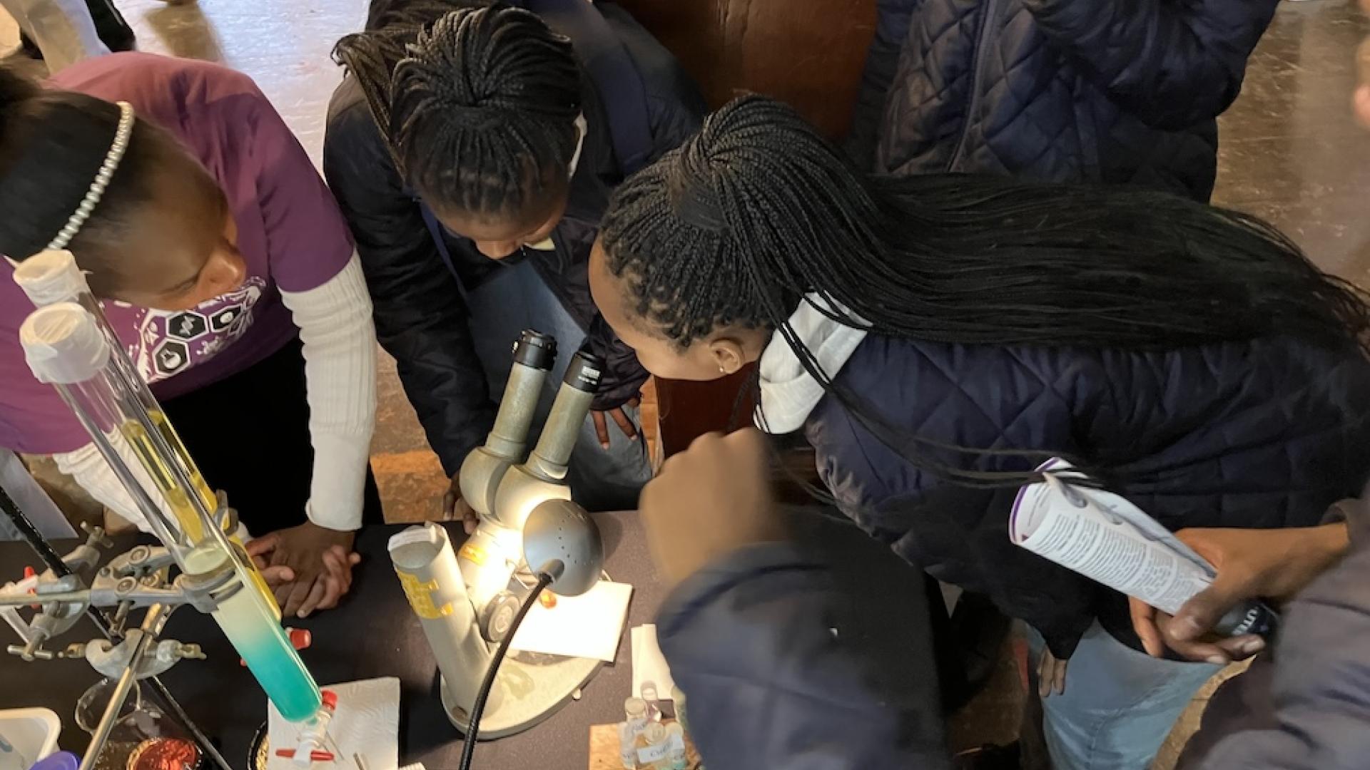 A postgraduate student shows interested learners a crystal using a microscope