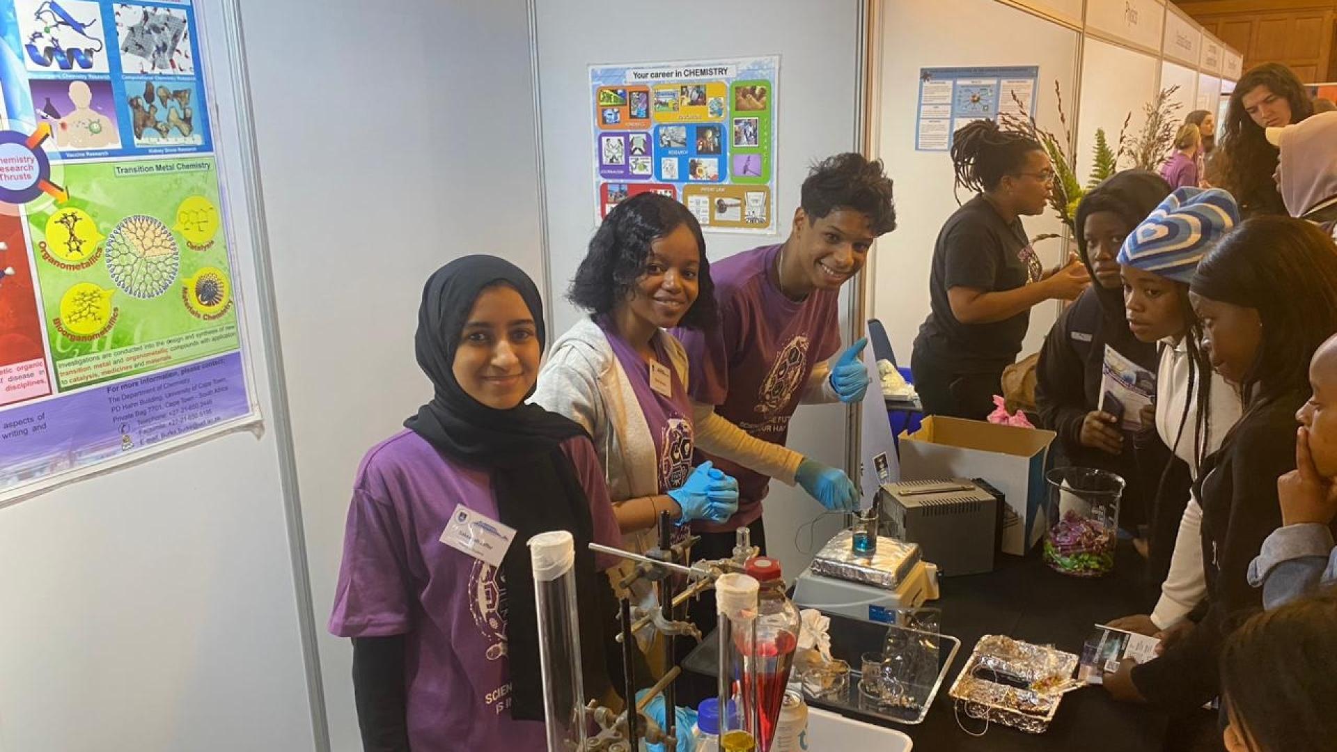 Three chemistry department postgraduate students pose in front of the chemistry exhibition