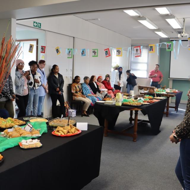 A room filled with people on the sides and tables filled with treats from different African countries.