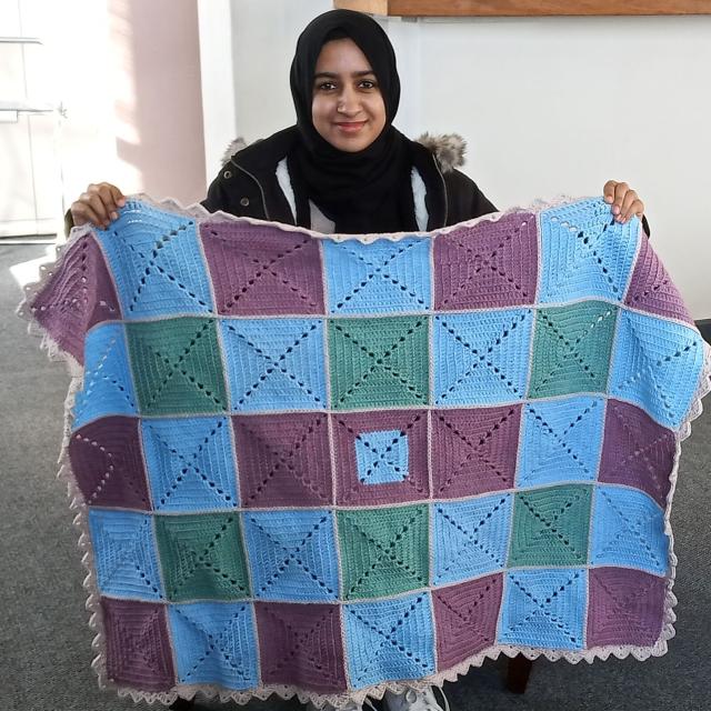 A student holding up her knitted blanket