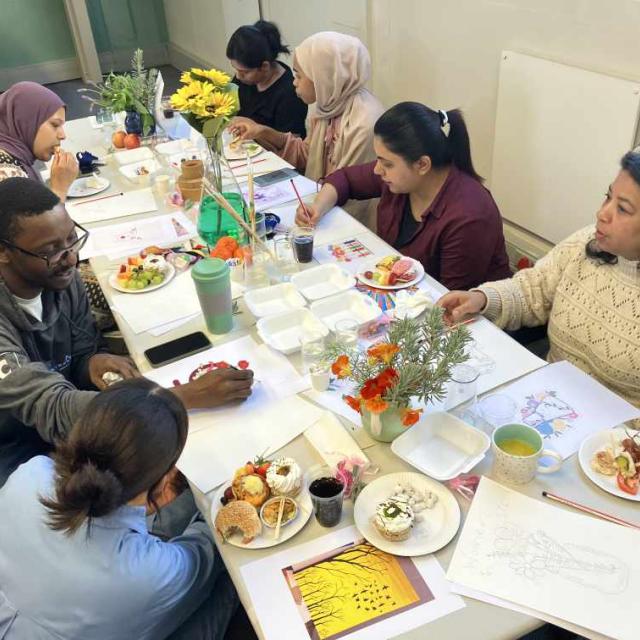 A group of people seated around a table with various dishes, beverages, and colorful flowers, in a casual dining setting.