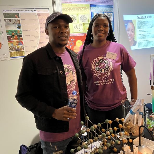 Two postgraduate students pose in front of the chemistry exhibition