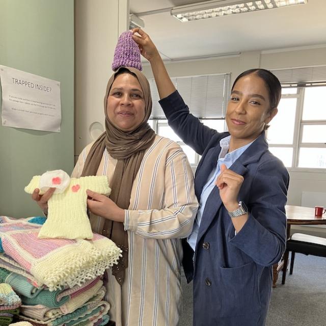 Woman playfully holds a knitted beanie over her colleague's head