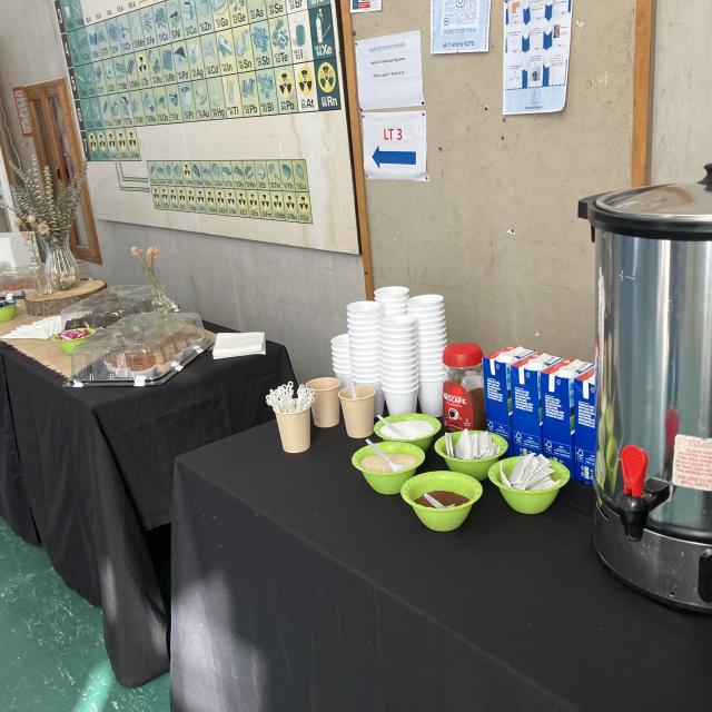 “Refreshment table with snacks and beverages in a hallway with informational posters.”