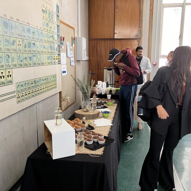 Classroom with students viewing a periodic table and a table with baked goods, likely during a science event.