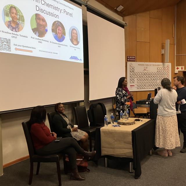 Panel discussion at a chemistry event with audience members and a whiteboard with notes.