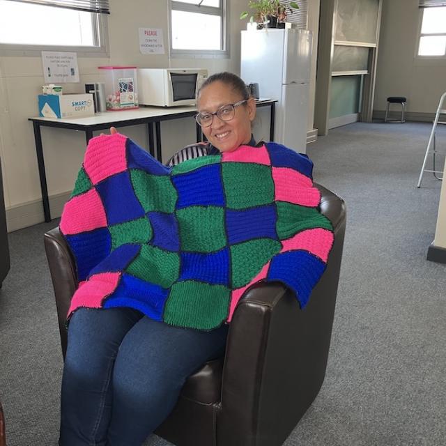 Woman holding a blue, green and pink knitted blanket