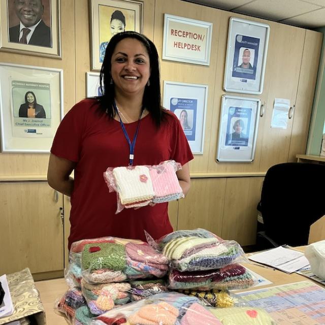 Woman standing in front of donated tiny knitted beanies and vests