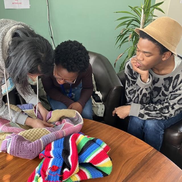 A woman shows another woman her knitting while a man looks on