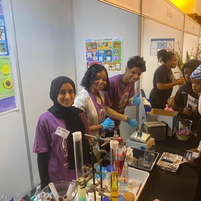 Three chemistry department postgraduate students pose in front of the chemistry exhibition