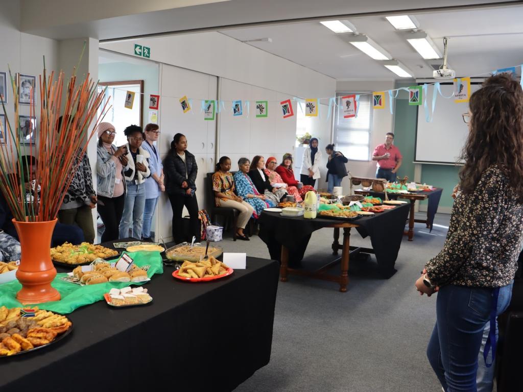 A room filled with people on the sides and tables filled with treats from different African countries.