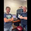 Picture of two smiling men standing in front of a mass spectrometer.